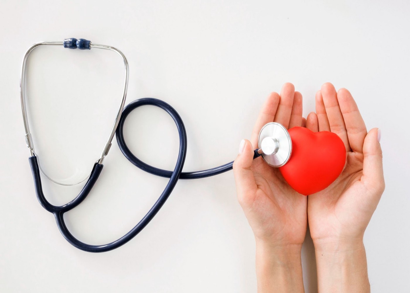 Stethoscope attached to a toy heart which is holded by a pair of hands.