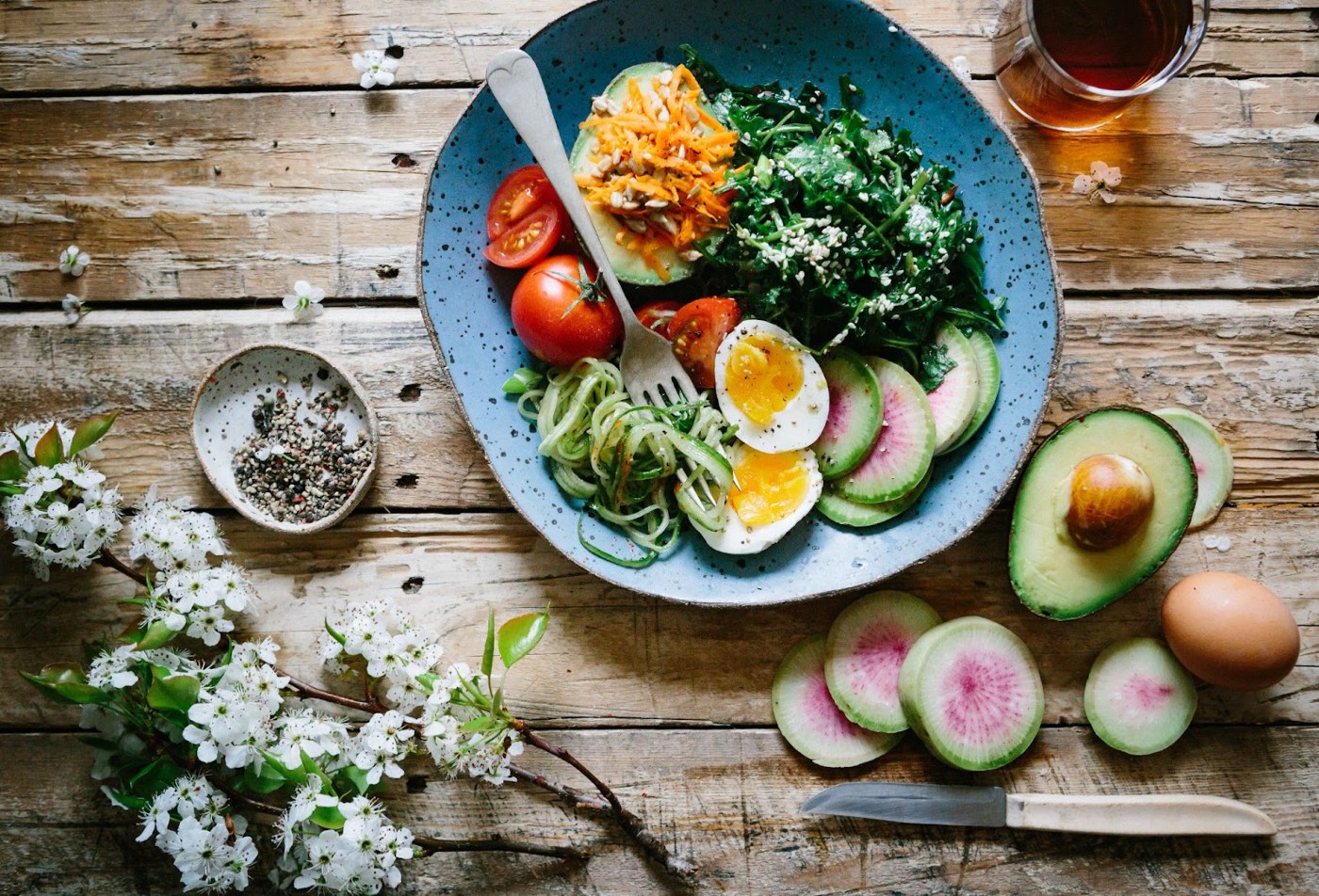 A table with a bowl of eggs and salads, tea, fruits and flowers.
