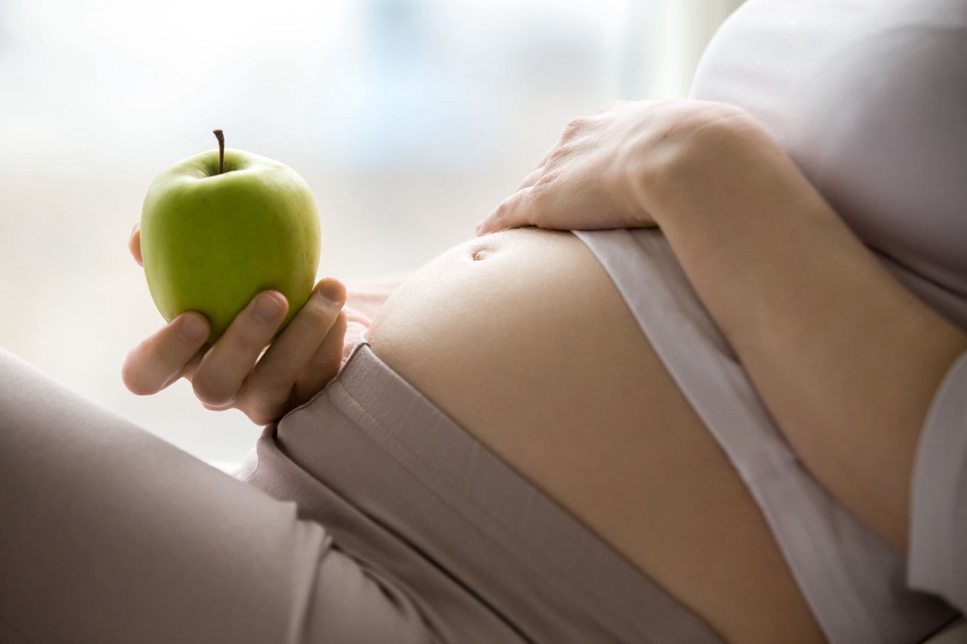 A pregnant woman holding a green apple.