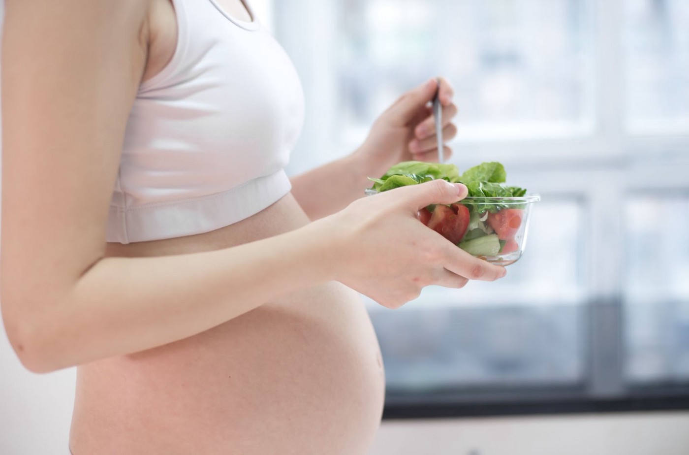 A pregnant woman holding a bowl of salads.